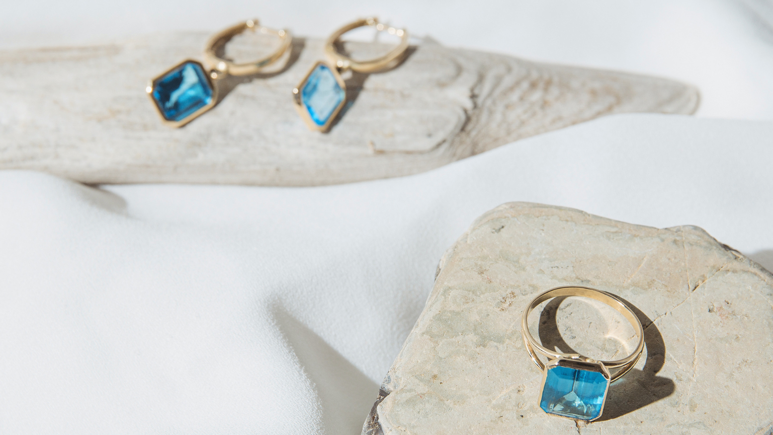 Goldring und Goldohrringe mit blauem Topaz auf grauem Stein
