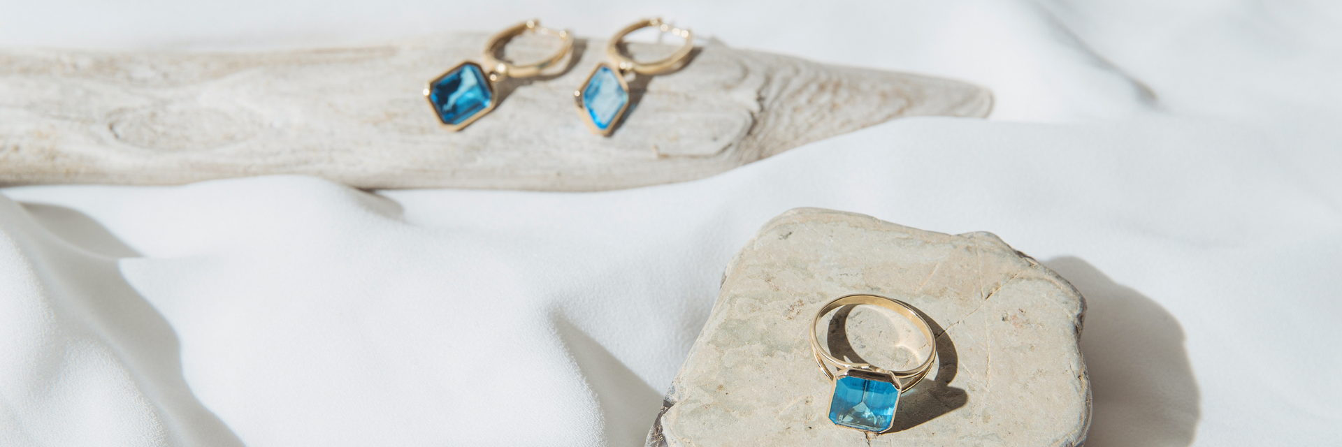 Goldring und Goldohrringe mit blauem Topaz auf grauem Stein